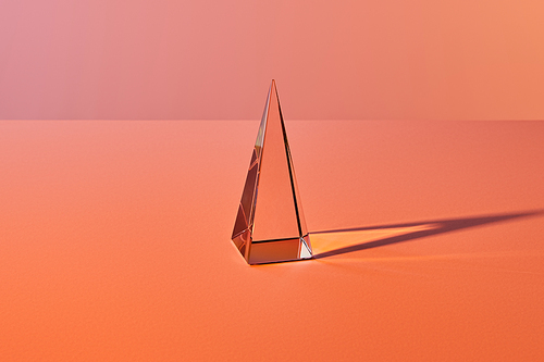 crystal transparent pyramid with light reflection on orange background