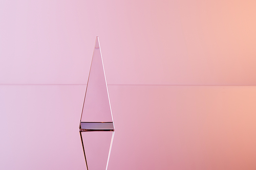 crystal transparent pyramid with reflection on pink background