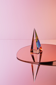 crystal transparent pyramid with reflection on round mirror on pink background