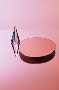 crystal transparent pyramid with reflection near round mirror on pink background