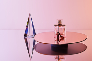 crystal transparent pyramid with reflection near perfume bottle on round mirror on pink background