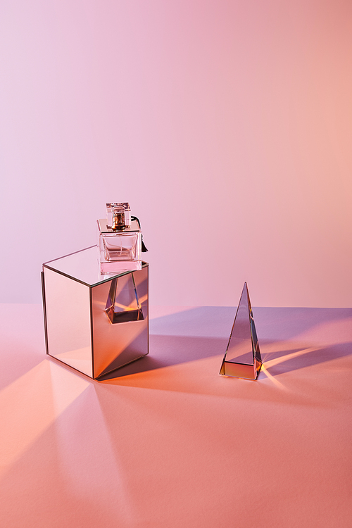 crystal transparent pyramid near perfume bottle on cube on pink background