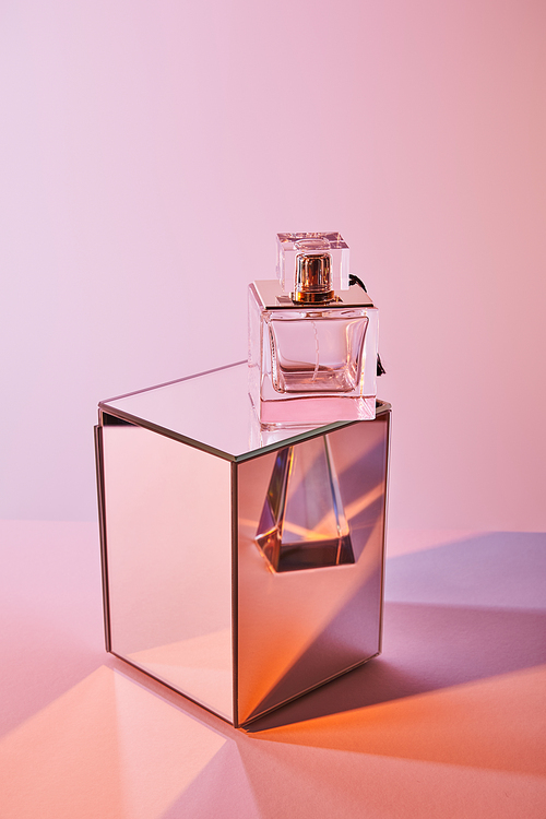 crystal transparent pyramid near perfume bottle on cube on pink background