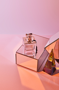 crystal transparent pyramid near perfume bottle and mirror cubes on pink background