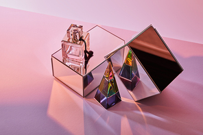 crystal transparent pyramid near perfume bottle and mirror cubes on pink background