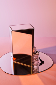 perfume bottle on round mirror with cube on pink background