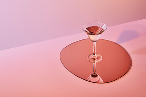 cocktail glass with liquid on mirror with reflection on pink background
