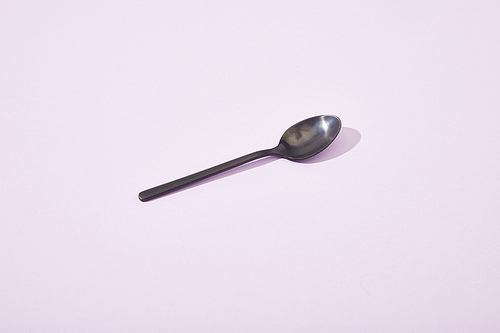 metal shiny black spoon on violet background