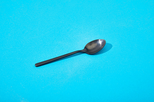 metal shiny black spoon on blue background