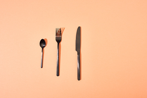 top view of metal shiny black fork, spoon and knife on orange background