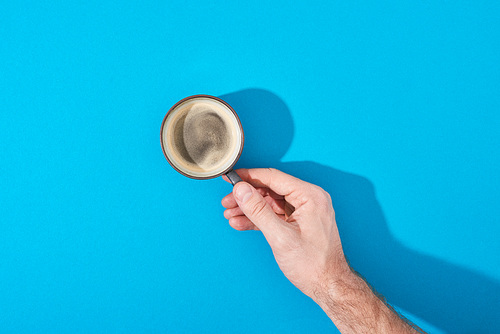 cropped view of man holding cup of fresh coffee on blue background