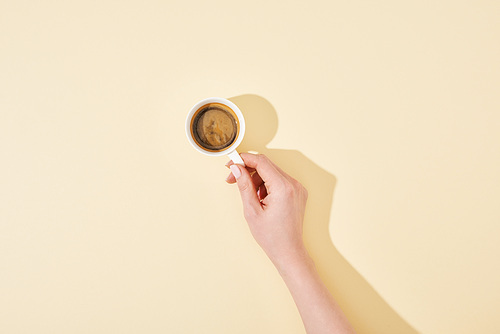 cropped view of woman holding cup of fresh coffee on beige background
