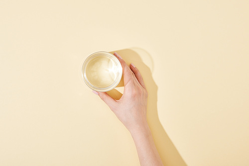 cropped view of woman holding glass of water on beige background