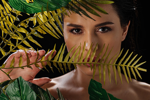 Portrait of beautiful woman  and covering face with fern leaf isolated on black