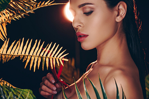 Sexy woman looking at anthurium near leaves on black background