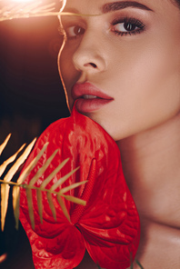 Portrait of woman with red anthurium and fern leaf  on dark background