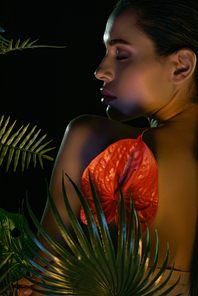 Back view of woman with closed eyes and red flower near leaves isolated on black