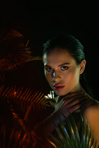 Beautiful girl touching neck and  with leaves on black