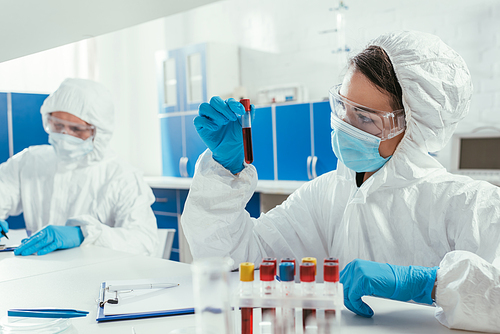 biochemist holding test tube with blood sample near colleague in laboratory