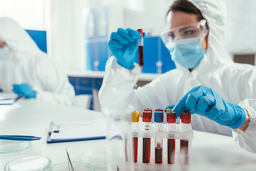 biochemist holding test tube with blood sample near colleague in laboratory