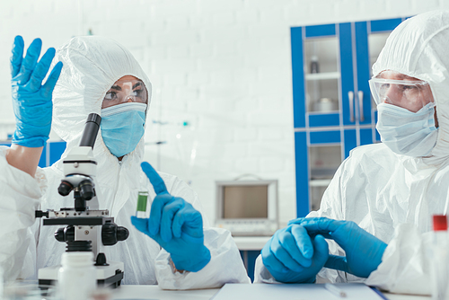two biochemists in hazmat suits talking in laboratory near microscope