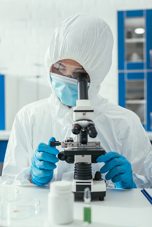 selective focus of biochemist in hazmat suit looking through microscope
