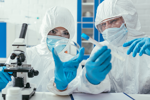 biochemists holding test tube and petri dish near microscope
