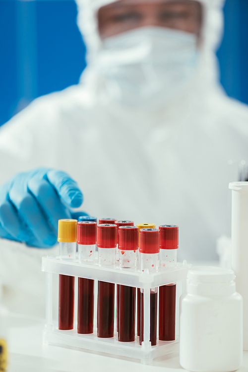 selective focus of test tubes with blood samples near biochemist in hazmat suit