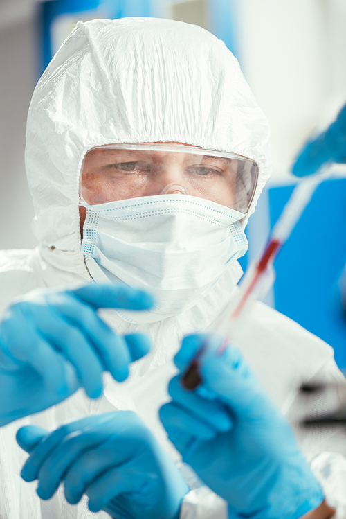 partial view of biochemist holding pipette and test tube with blood sample near colleague