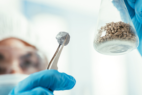 selective focus of biochemist holding small stone with tweezer and flask with gravel