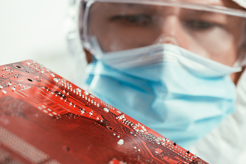 selective focus of engineer in medical mask and goggles holding computer motherboard