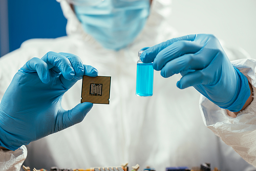 cropped of engineer holding computer microchip and glass container with blue liquid