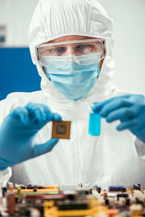 selective focus of engineer holding microchip and glass container with blue liquid near computer motherboard