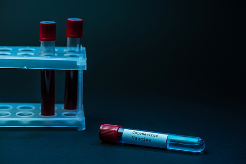 Coronavirus vaccine near test tube rack with blood samples on dark