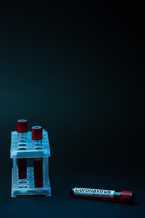 Coronavirus blood sample near test tube rack with tubes on dark background