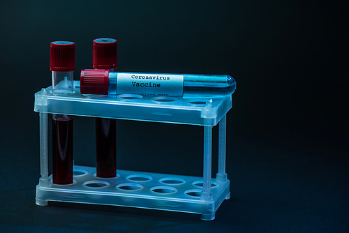 Coronavirus vaccine on test tube rack with sample tubes with blood on dark background