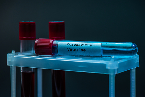 Coronavirus vaccine on test tube rack with sample tubes with blood on dark