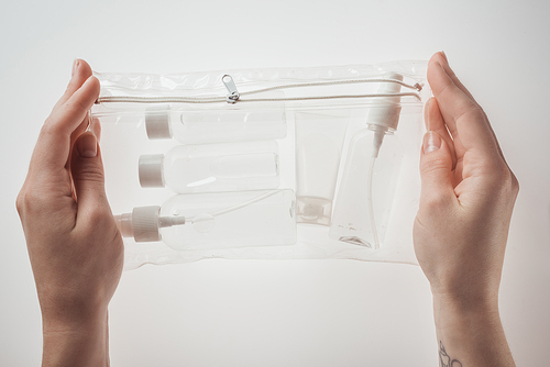 cropped view of woman holding cosmetic bag with bottles and tube on white background