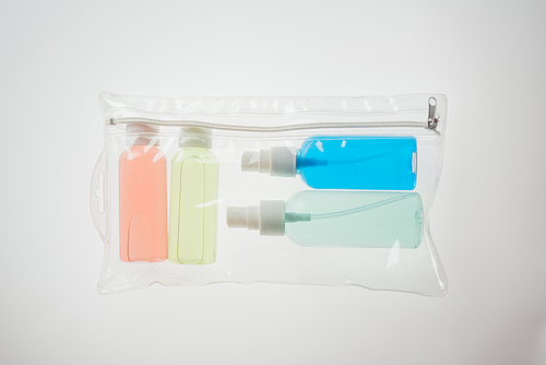 top view of colorful bottles with liquids in cosmetic bag on white background
