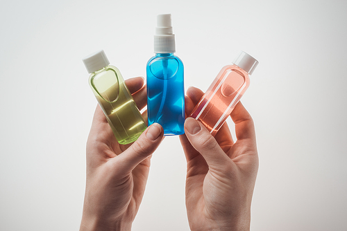 cropped view of woman holding bottles with liquids on white background