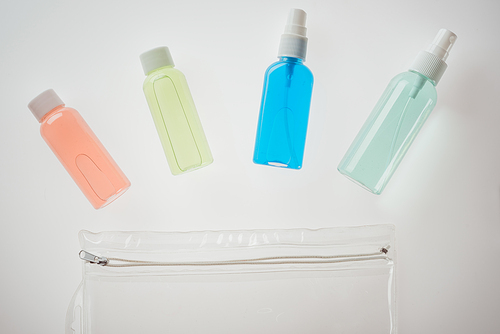 top view of colorful bottles with liquids and cosmetic bag on white background