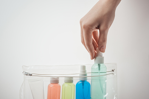 cropped view of woman putting bottle with liquid to cosmetic bag on white background