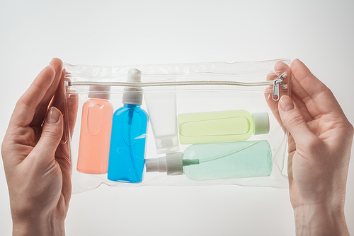cropped view of woman holding cosmetic bag with colorful bottles with liquids on white background
