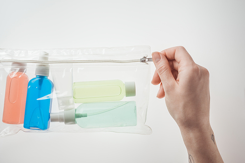 cropped view of woman holding cosmetic bag with colorful bottles with liquids on white background