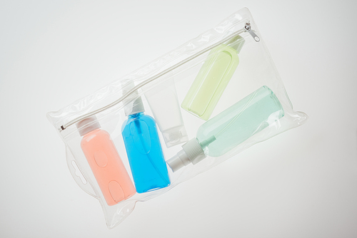 top view of cosmetic bag with colorful bottles with liquids on white background