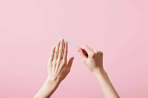 Cropped view of woman filing fingernails with nail file isolated on pink
