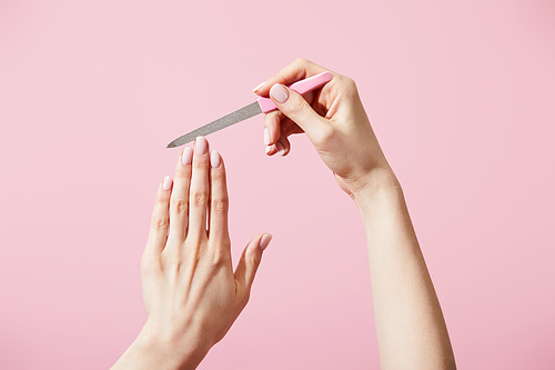 Partial view of woman filing fingernail with nail file isolated on pink