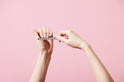 Cropped view of woman filing nails with nail file isolated on pink
