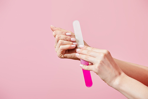 Partial view of woman doing manicure with nail file isolated on pink