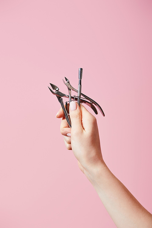 Cropped view of female hand with cuticle pusher and nippers isolated on pink